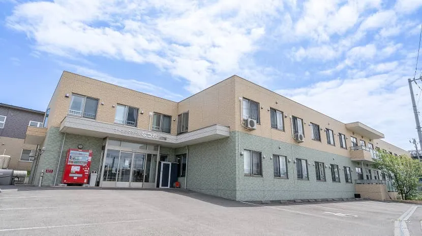 介護施設の建物外観。2階建てモダンな設計で、玄関前に駐車スペースがある